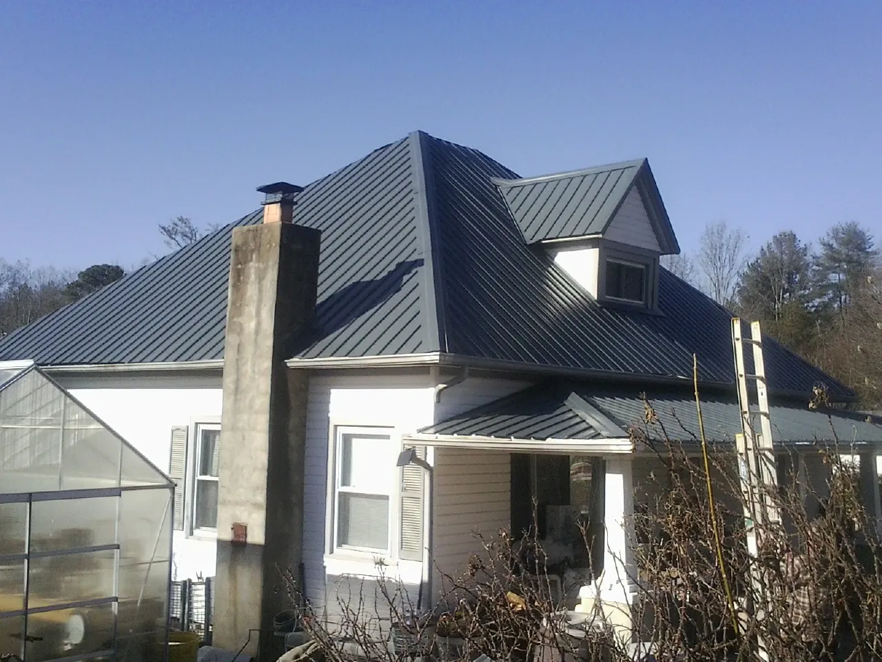 Dark blue standing seam metal roof on a white farmhouse with dormer — Slate & Tile Roof Repair by Roofing Brothers in El Paso