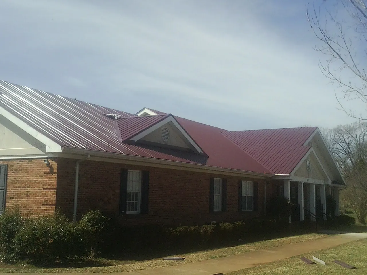 Red metal roof with gabled entries on a long brick building, from a Hail Damage Roof Repair job in El Paso