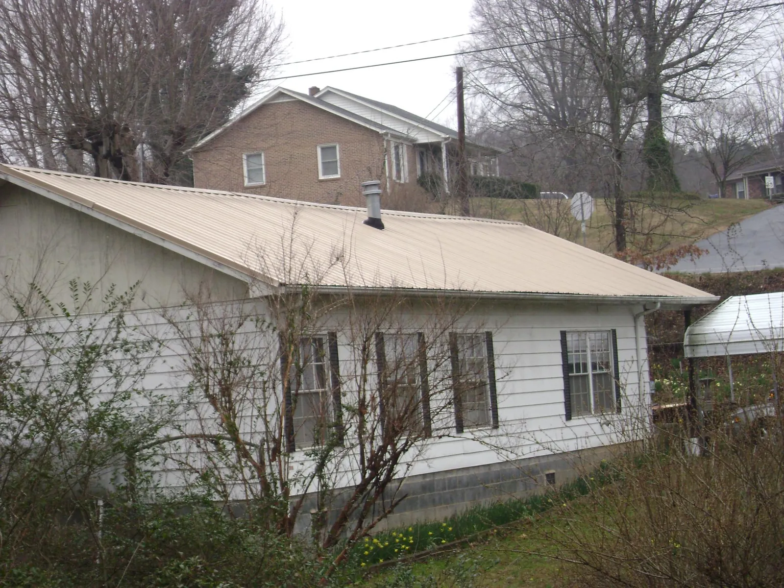 Tan metal roof on a white sided house set into a hillside — Commercial Roofing by Roofing Brothers in El Paso